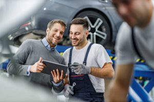 Happy customer and auto mechanic using touchpad in a workshop. Happy manager and auto mechanic cooperating while using digital tablet in a repair shop. Maintenance manager stock pictures, royalty-free photos & images