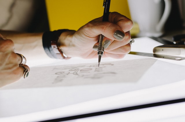 A lady drafting a design on a sheet with the help of a pen.