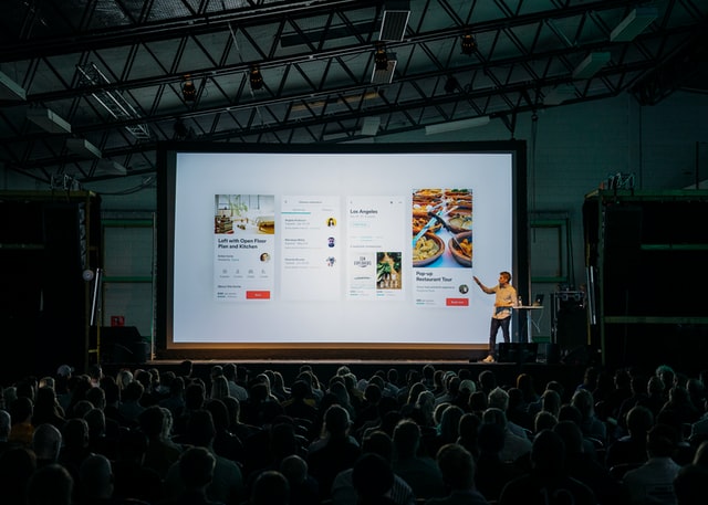 Man presenting on a screen to a large audience.